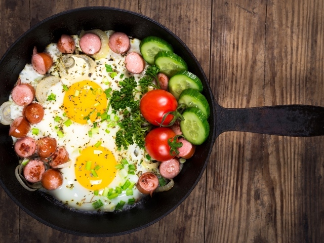 Яичница в сковороде с овощами и кусочками сосиски