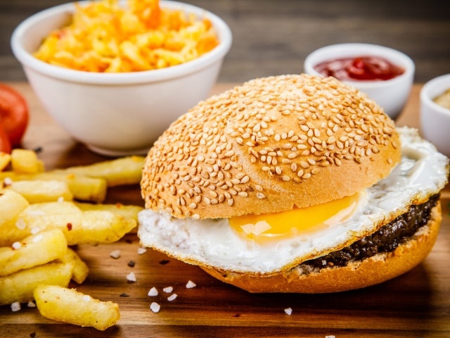 Гамбургер с яичницей на столе с картофелем фри и соусом