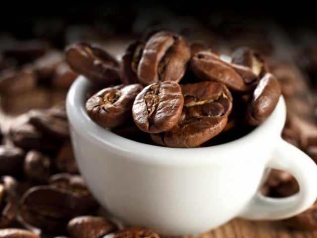 Много кофейных зерен в белой чашке на столе