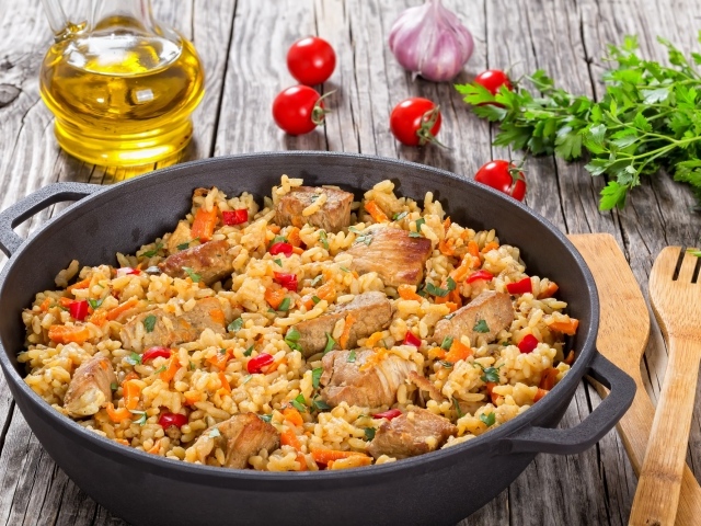 Плов с мясом на столе с помидорами и зеленью петрушки