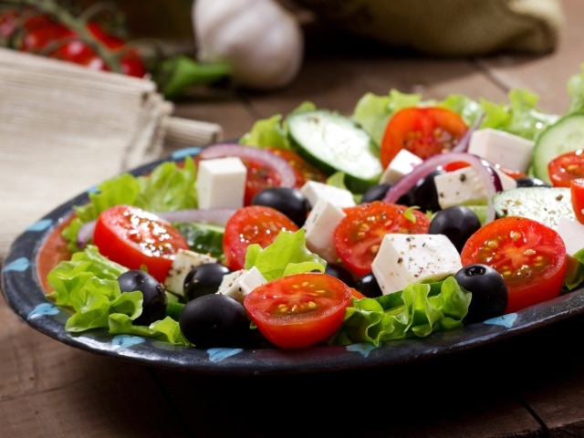 Салат с помидорами, огурцами, оливками, кусочками сыра и луком на листьях салата