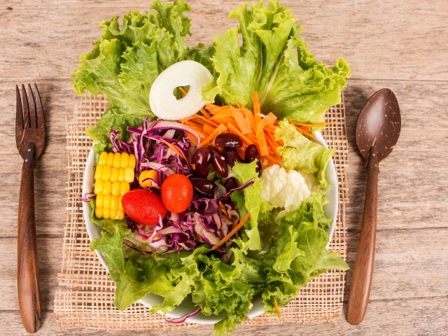 Салат с овощами и зелеными листьями салата в тарелке на столе со столовыми приборами