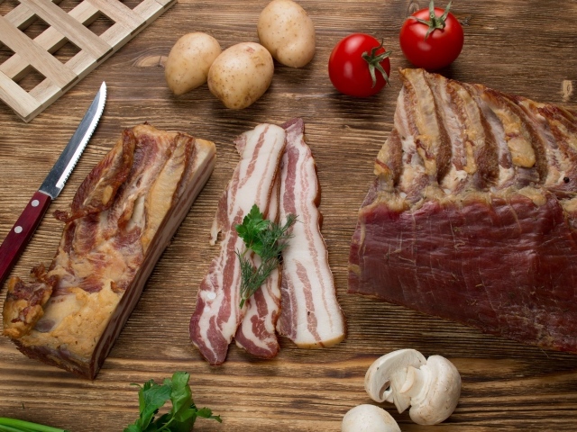 Нарезанное сало на столе с картофелем, помидорами и грибами 