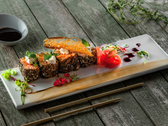 Суши на тарелке на деревянном столе с соусом