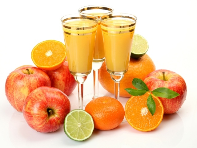 Три бокала сока на столе с яблоками и апельсинами на белом фоне