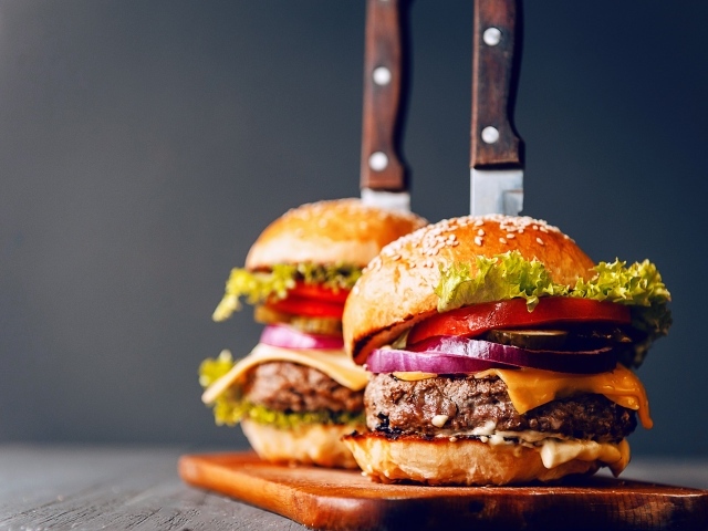 Два гамбургера с ножами на разделочной доске 