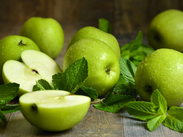 Зеленые яблоки в каплях воды на столе с мятой