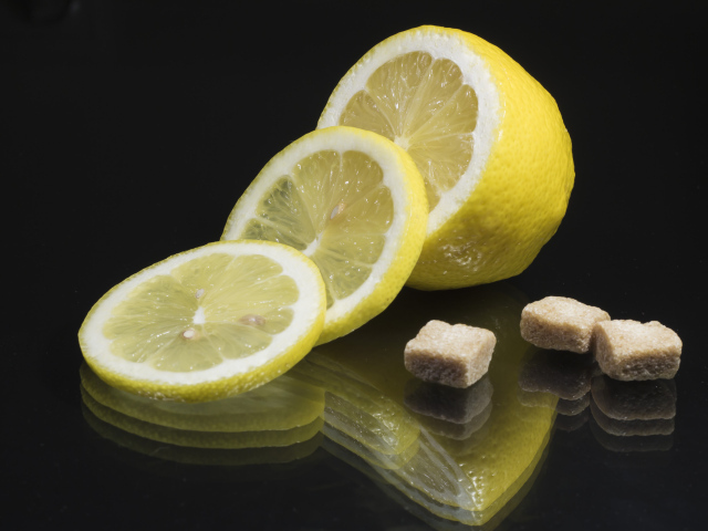 Нарезанный лимон с кусочками коричневого сахара на черном фоне