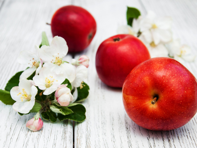 Три красных яблока с цветами на деревянной поверхности