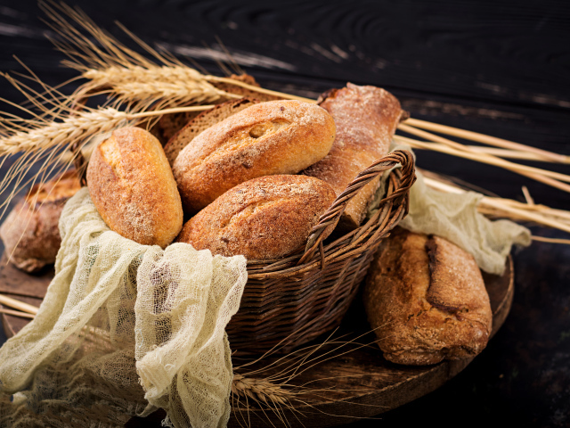 Свежая выпечка в корзине на столе с колосьями пшеницы