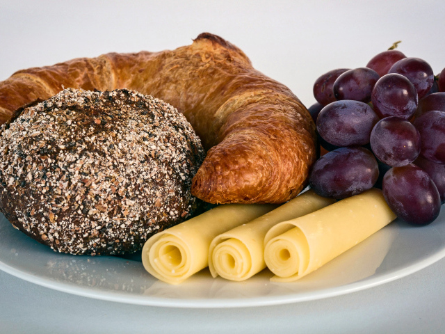 Свежая выпечка с сыром и розовым виноградом на белой тарелке 