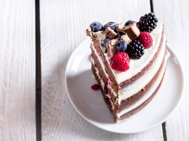 Кусок торта с ягодами малины и черники на блюдце