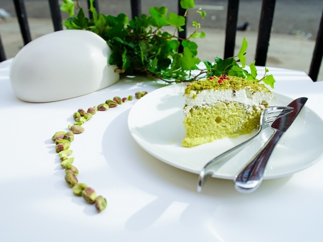 Кусок фисташкового торта на тарелке с вилкой и ножом