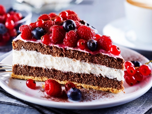 Аппетитный кусок торта на тарелке с ягодами малины, красной смородины и черники
