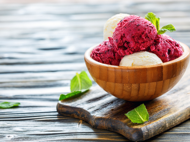 Шарики фруктового и ванильного мороженого в деревянной миске на столе