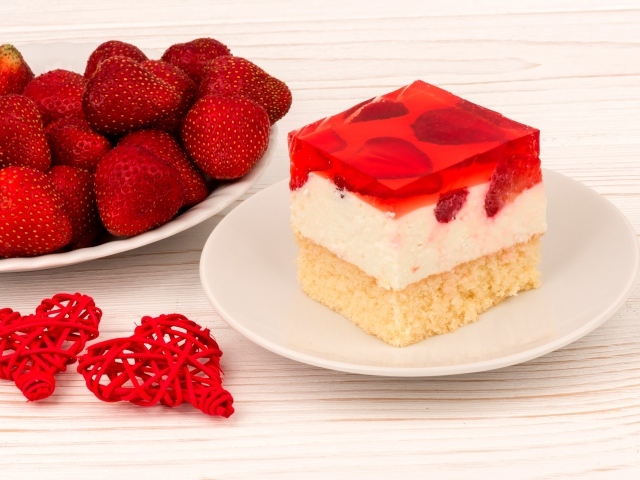 Пирожное на столе с клубникой и красными плетеными сердечками