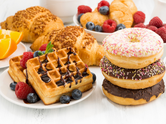 Круассаны, вафли и пончики на столе с ягодами