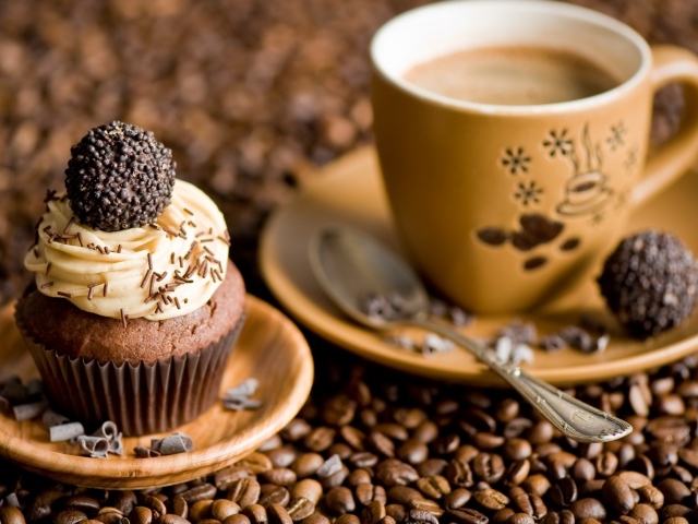 Кекс с кремом и чашкой кофе стоят на кофейных зернах 