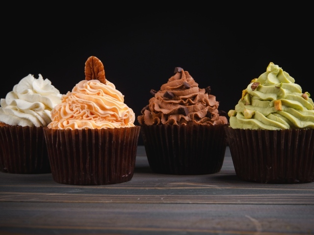 Четыре аппетитных капкейка с кремом на черном фоне
