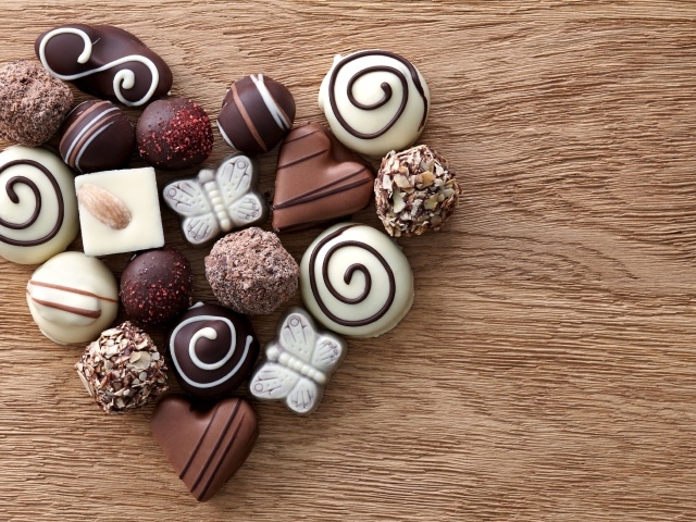 Сердце из шоколадных конфет ассорти на деревянном столе