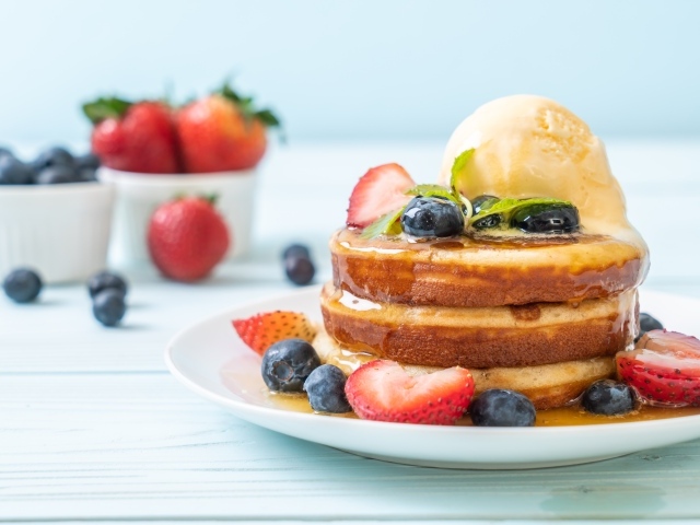 Оладья и медом, мороженым и ягодами черники и клубники на столе