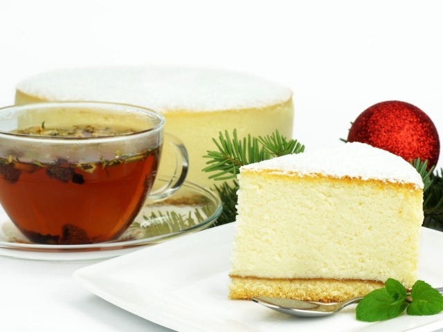 Кусок чизкейка на белой тарелке с чашкой чая на белом фоне