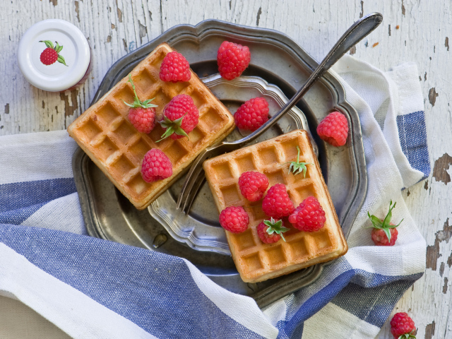 Сладкие вафли с ягодами малины на столе 