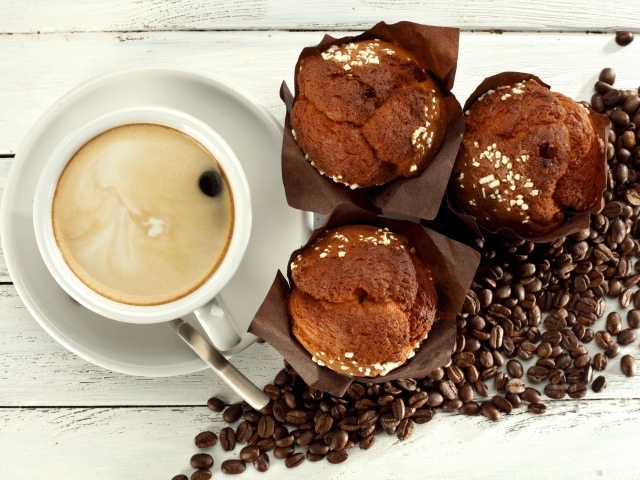 Чашка кофе с кексами и кофейными зернами на столе