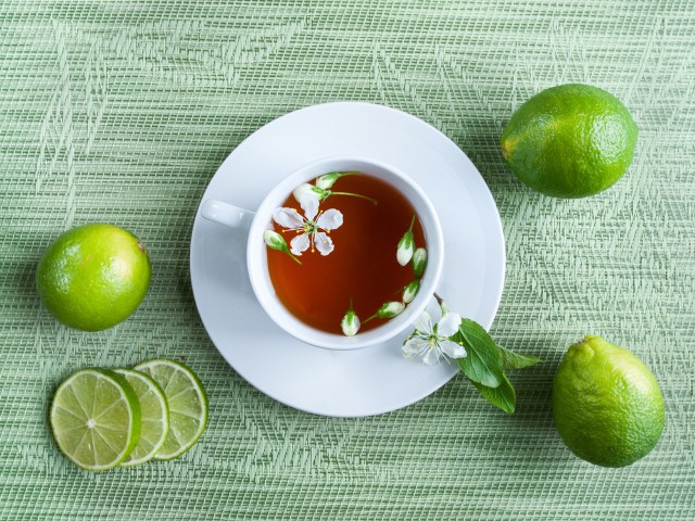 Чашка чая с зелеными лаймами на столе
