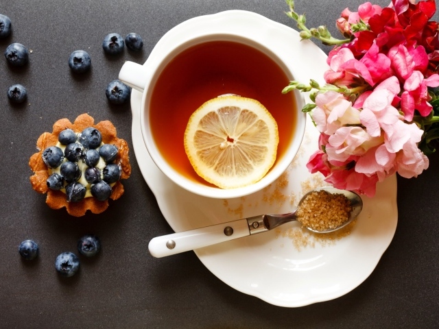 Чашка чая с лимоном на столе с кексом и цветами