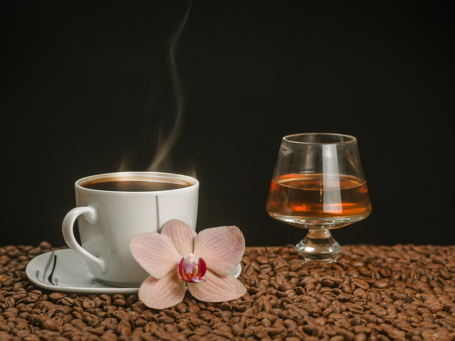 Ароматная чашка кофе на столе с бокалом виски, кофейными зернами и цветком орхидеи