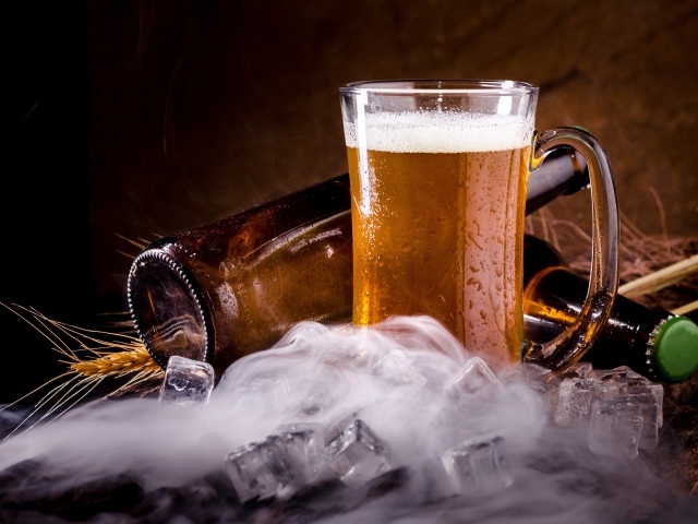 Бутылки пива с бокалом и кубиками льда на столе