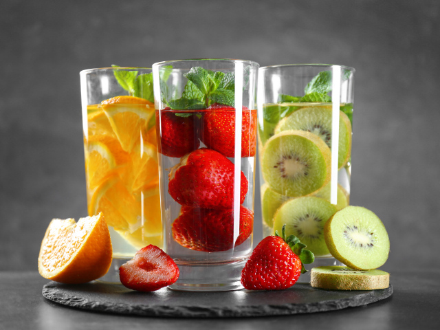 Напитки в стаканах с клубникой, киви и апельсинами на сером фоне