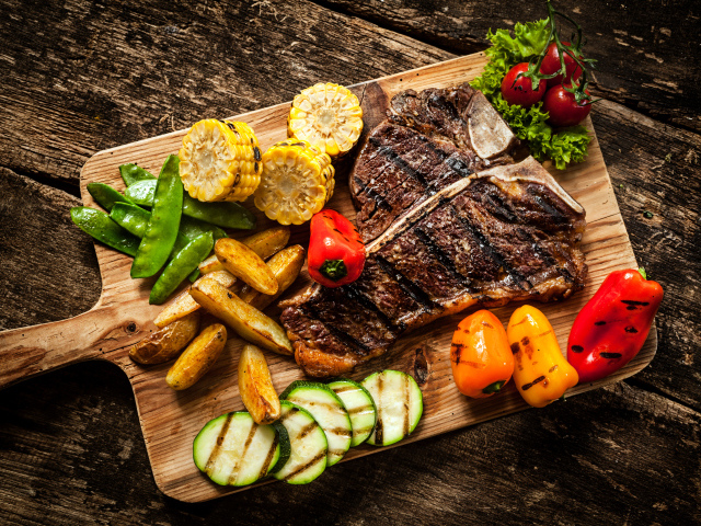 Кусок мяса на разделочной доске с овощами