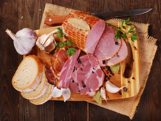 Аппетитная ветчина, чеснок и кусочки хлеба на разделочной доске
