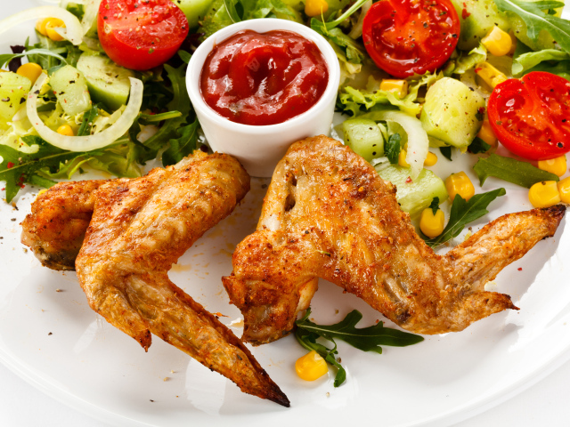 Жареные куриные крылышки с овощами и кетчупом на белой тарелке