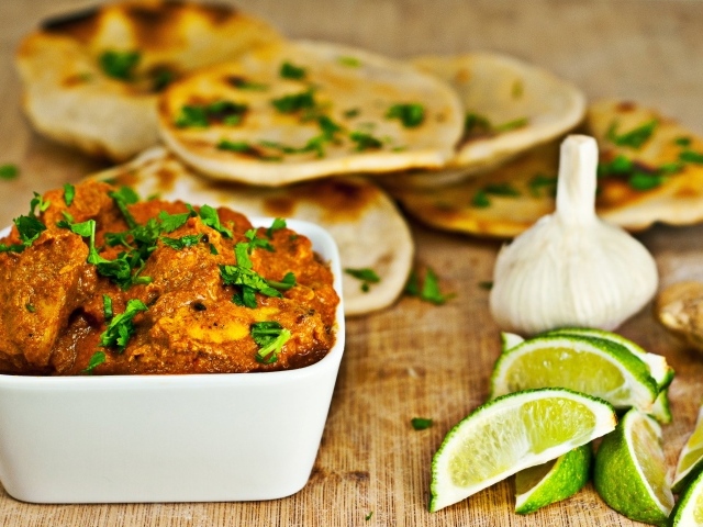 Мясное блюдо на столе с лепешками, кусочками лайма и чесноком