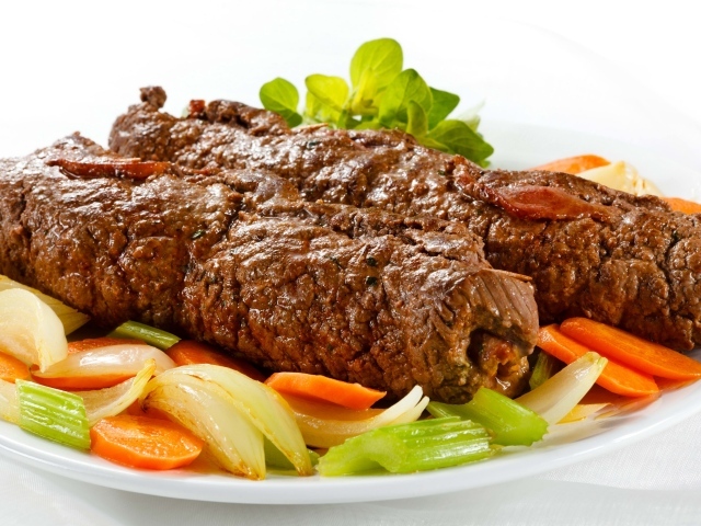 Свинина на тарелке с овощами на белом фоне