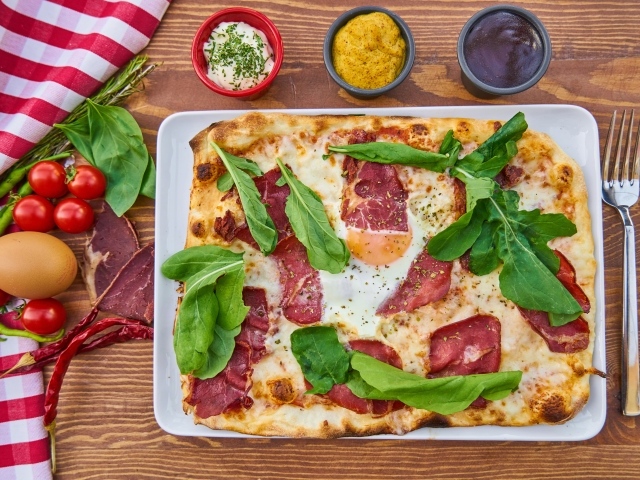 Пицца с беконом и зелеными листьями базилика на столе 