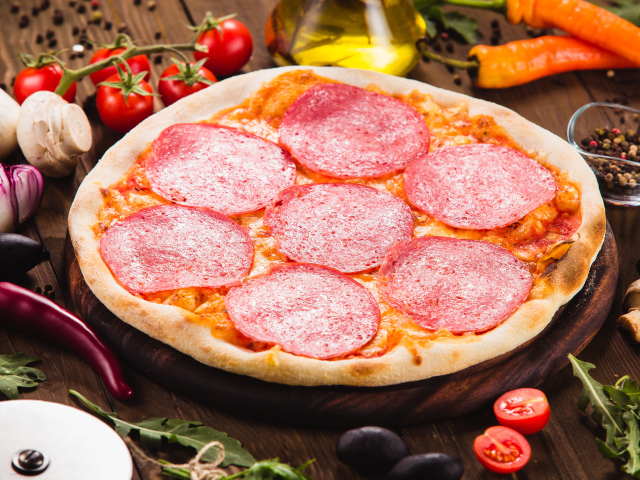 Пицца с салями на столе с овощами 