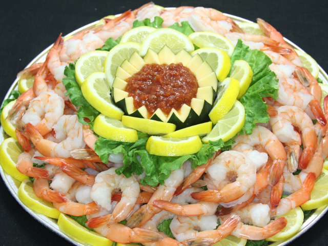 Вареные креветки с лимоном и соусом на большой тарелке