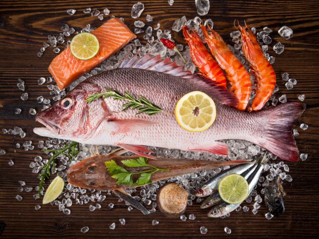 Свежая рыба с креветками и кусочками лимона лежит на кусочках льда