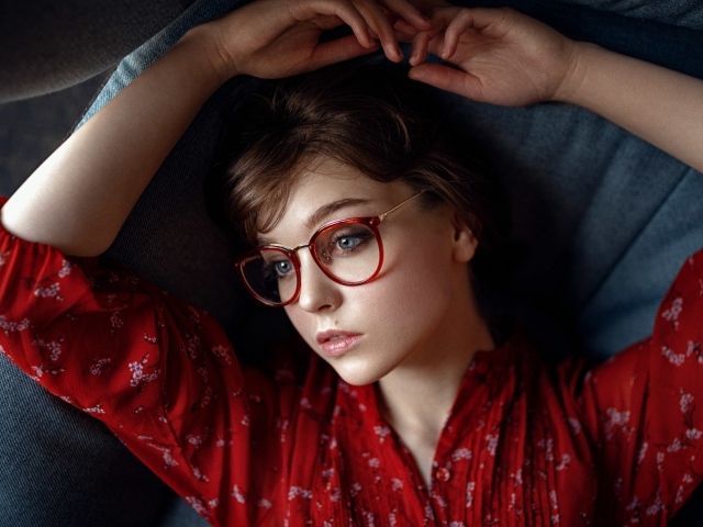 Молодая девушка в очках лежит на диване 