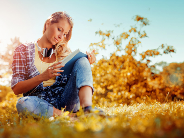 Молодая девушка читает книгу на желтой траве осенью