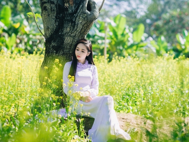 Красивая девушка азиатка сидит в белом платье под деревом