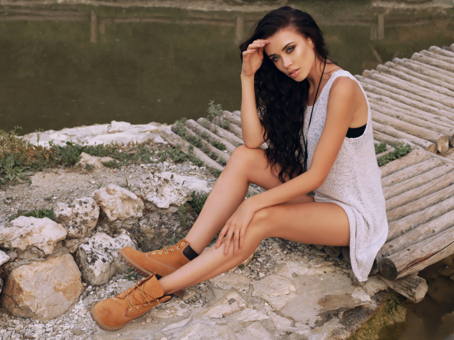 Красивая девушка брюнетка сидит у воды на мостике