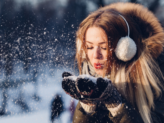 Красивая девушка сдувает снег с ладоней зимой