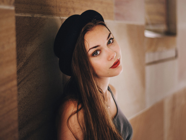 Красивая девушка в черной шляпе у стены 