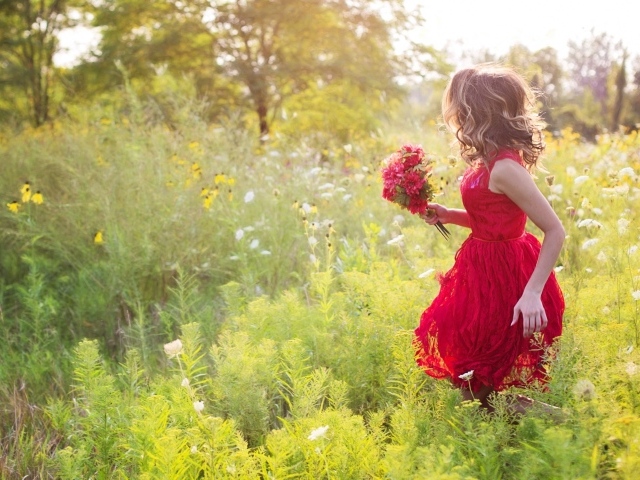 Красивая девушка в красном платье гуляет с букетом в руках по траве