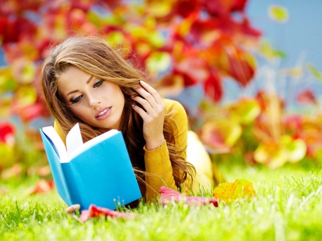 Красивая девушка читает книгу лежа на зеленой траве